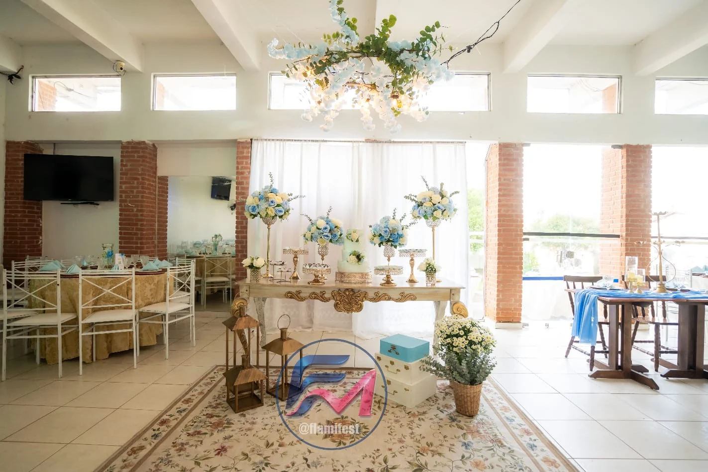 Decoração de evento com mesa de doces, flores e lustre em salão iluminado